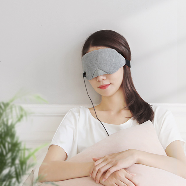 흰색 티셔츠를 입은 여성이 앉아서 온열 안대를 쓰고 있으며 정면을 보는 착용 모습
