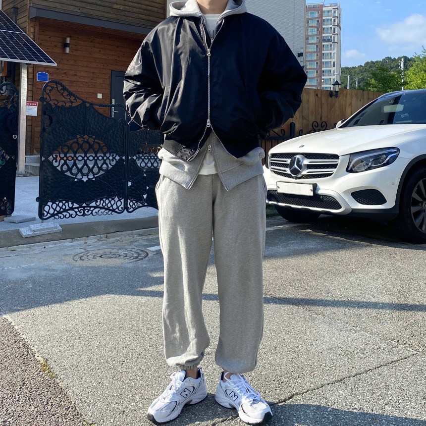 Black cropped bomber layered over a gray hoodie with loose gray sweatpants and white running shoes
