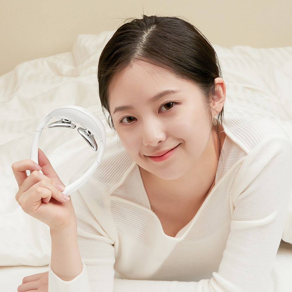 침대에서 넥큐어를 정면으로 향하게 들고 있는 여성의 모습으로 제품 전면의 곡선 디자인을 표현함