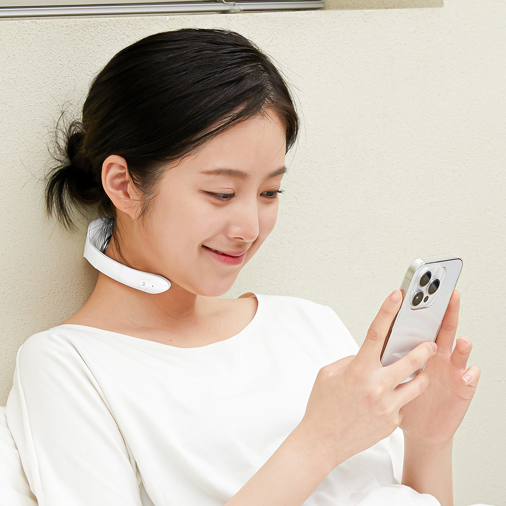 목에 착용한 흰색 넥큐어 마사지기로 스마트폰을 보고 있는 장면으로, 실제 사용 중인 모습과 제품의 목 부착 형태를 보여줌