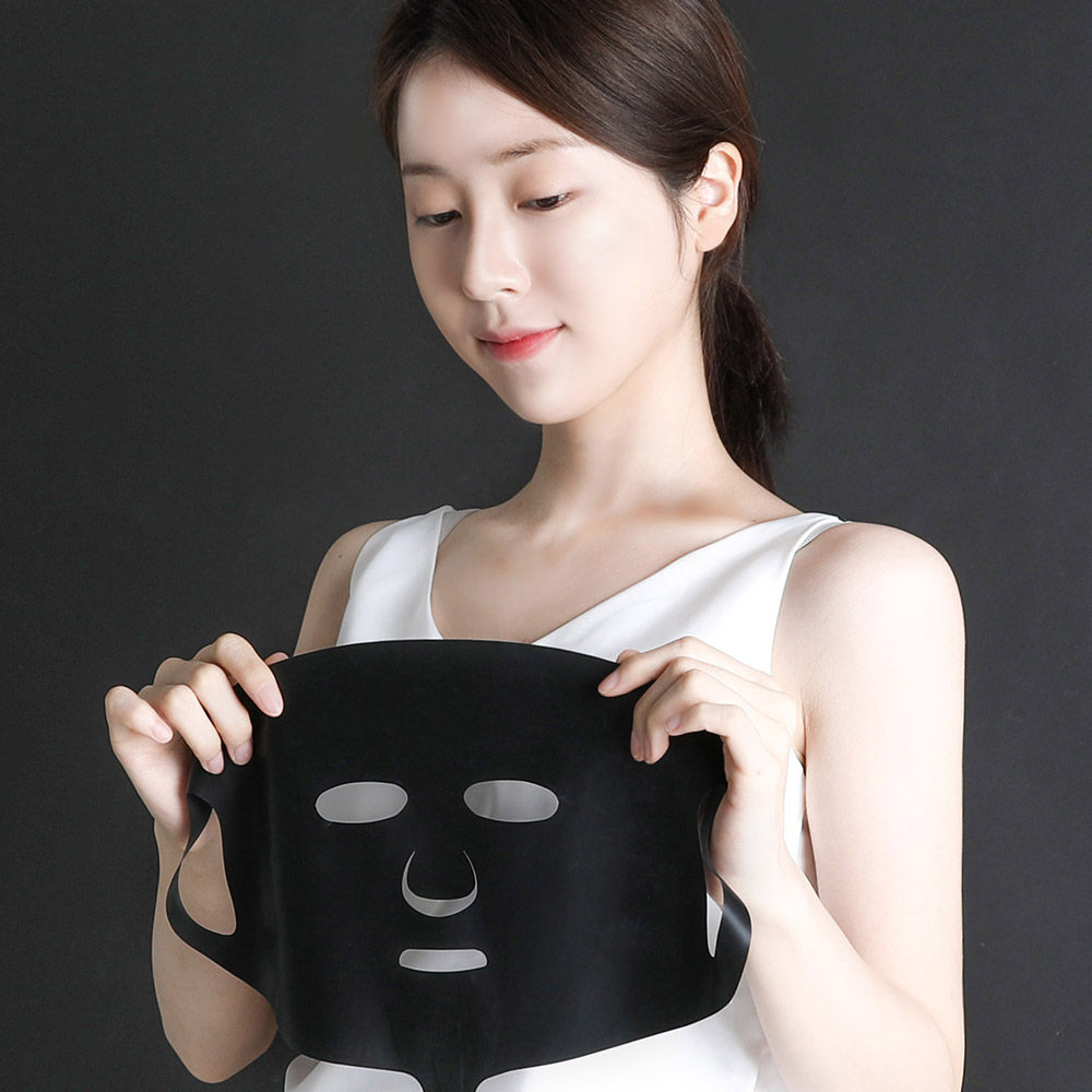 흰 민소매 옷을 입은 여성이 검은색 마스크팩 모양의 기기를 양손으로 들고 있는 모습