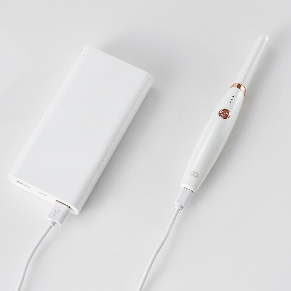 흰 수납 박스와 로즈골드 가전 장식이 있는 흰색 고데기, USB 연결 케이블이 함께 놓여 있음
