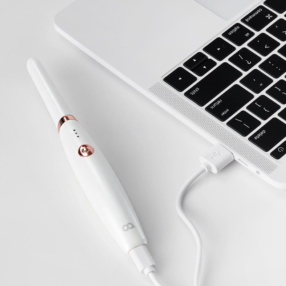 노트북 키보드 옆에 놓인 고데기와 USB 충전 케이블, 휴대하기 쉬운 콤팩트한 크기를 보여줌