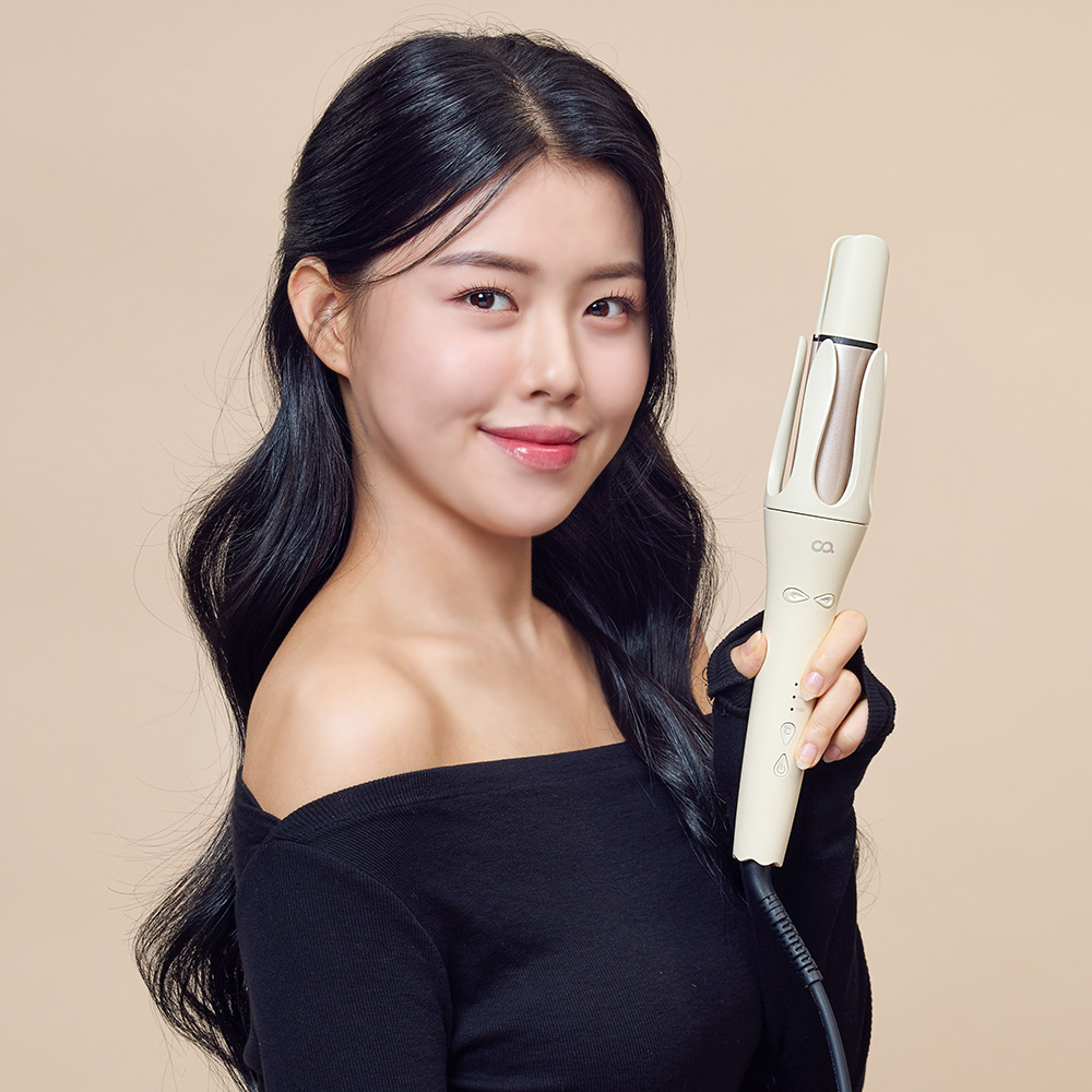 베이지색 자동 회전 고데기를 손에 들고 있는 여성의 어깨부터 얼굴까지의 정면 사진