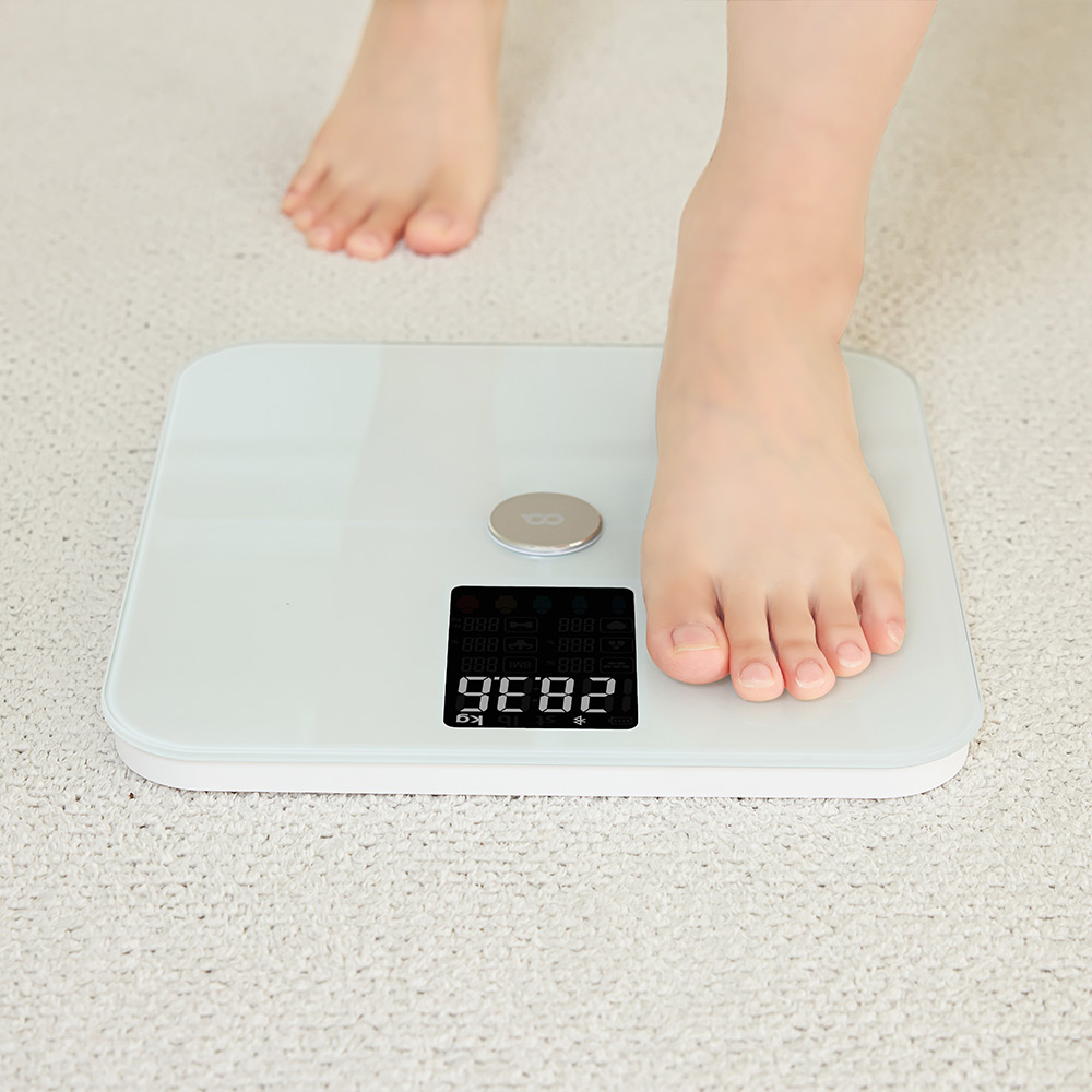 하얀색 바닥 위에 서 있는 발이 흰색 체중계 위에 올려져 있고 디스플레이에 체중 수치가 표시되는 모습