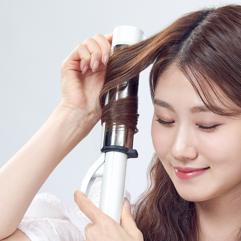고데기의 회전식 열 드럼 부분에 머리카락을 감싸 스타일링하는 장면을 근접으로 촬영