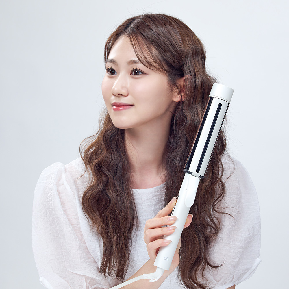 흰색과 검은색 고데기를 들고 있는 여성이 긴 웨이브 머리를 보여주는 모습