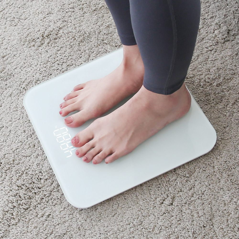 체중계 위에 양발을 올린 사람의 하반신을 위에서 촬영한 구도로 LED 수치가 보이는 장면