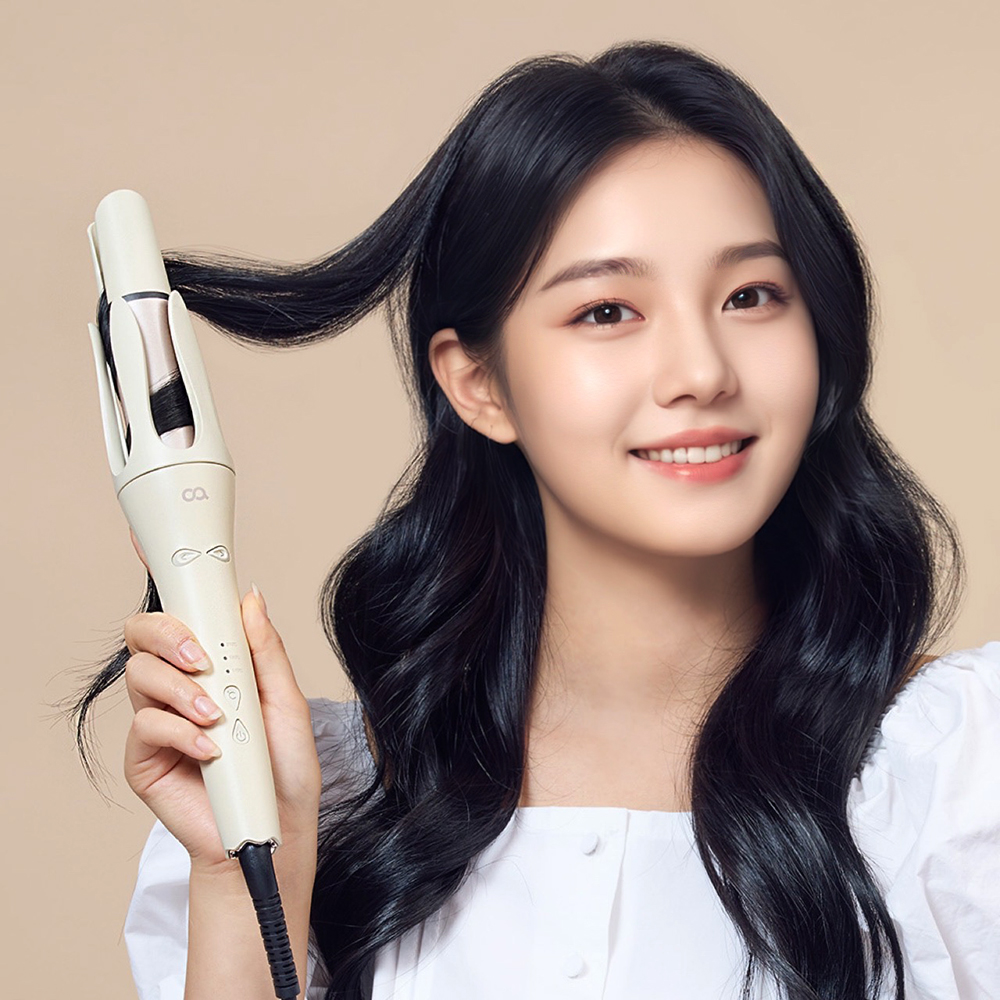 베이지색 자동 회전 봉 고데기를 들고 웨이브 스타일의 검은머리를 연출한 여성의 측면