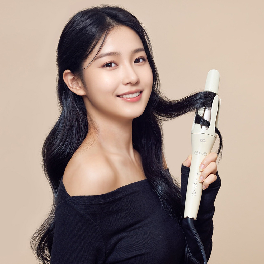 베이지 자동 봉 고데기를 들고 있는 여성이 손으로 머리에 웨이브를 만드는 사용 장면