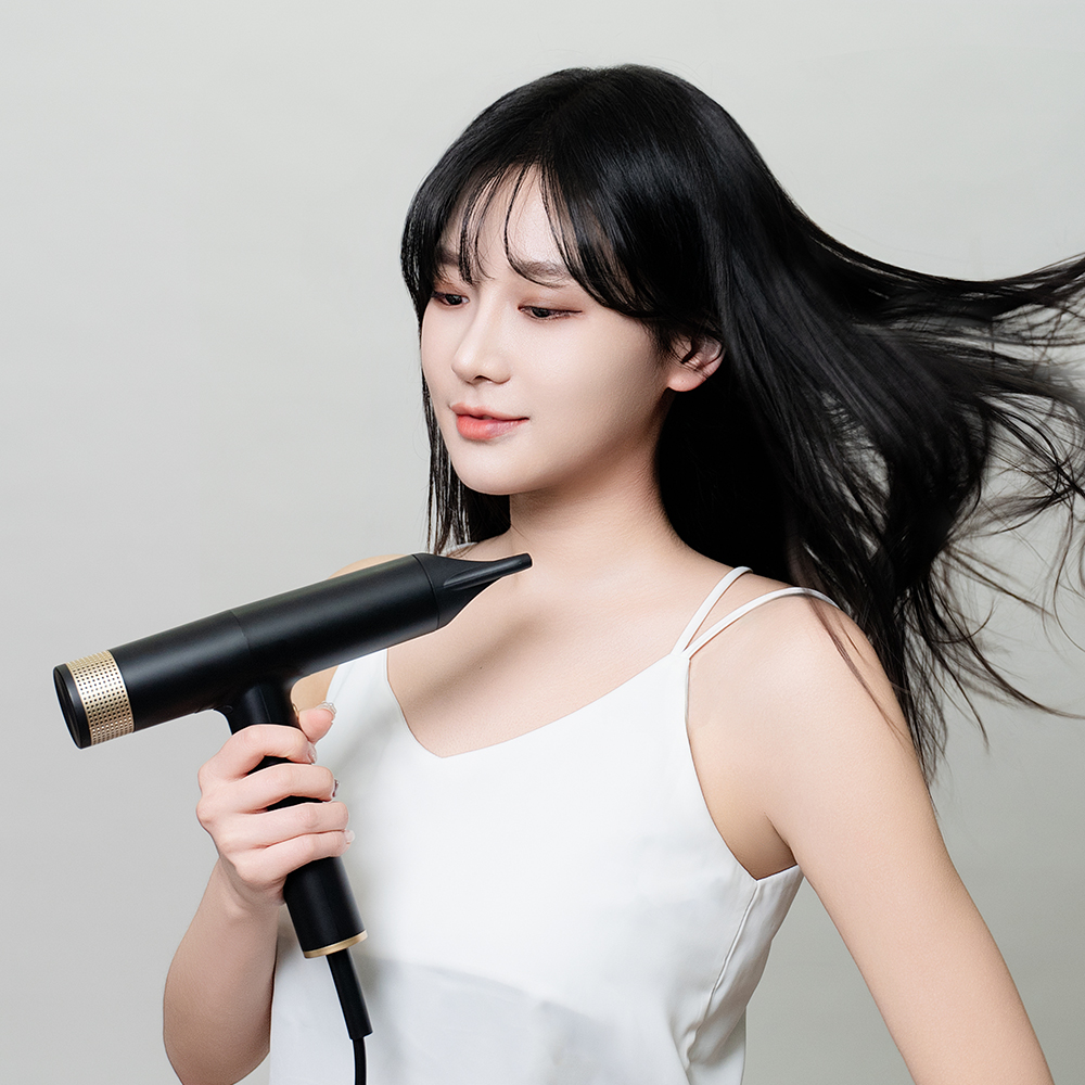 여성이 흰색 민소매 상의를 입고 검은색 미니 드라이기를 손에 들어 긴 검은 머리에 사용하고 있는 모습