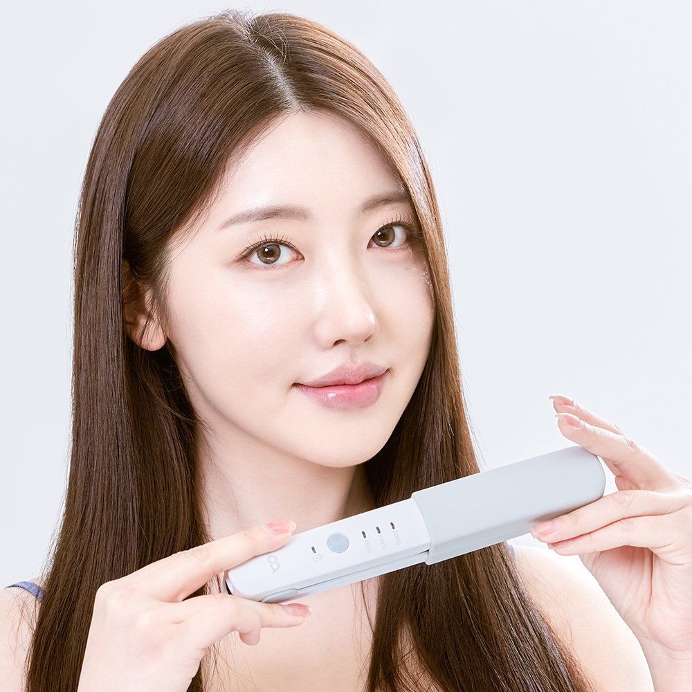 여성이 흰색 무선 고데기를 손에 들고 본인의 긴 머리를 스타일링하는 실제 사용 모습