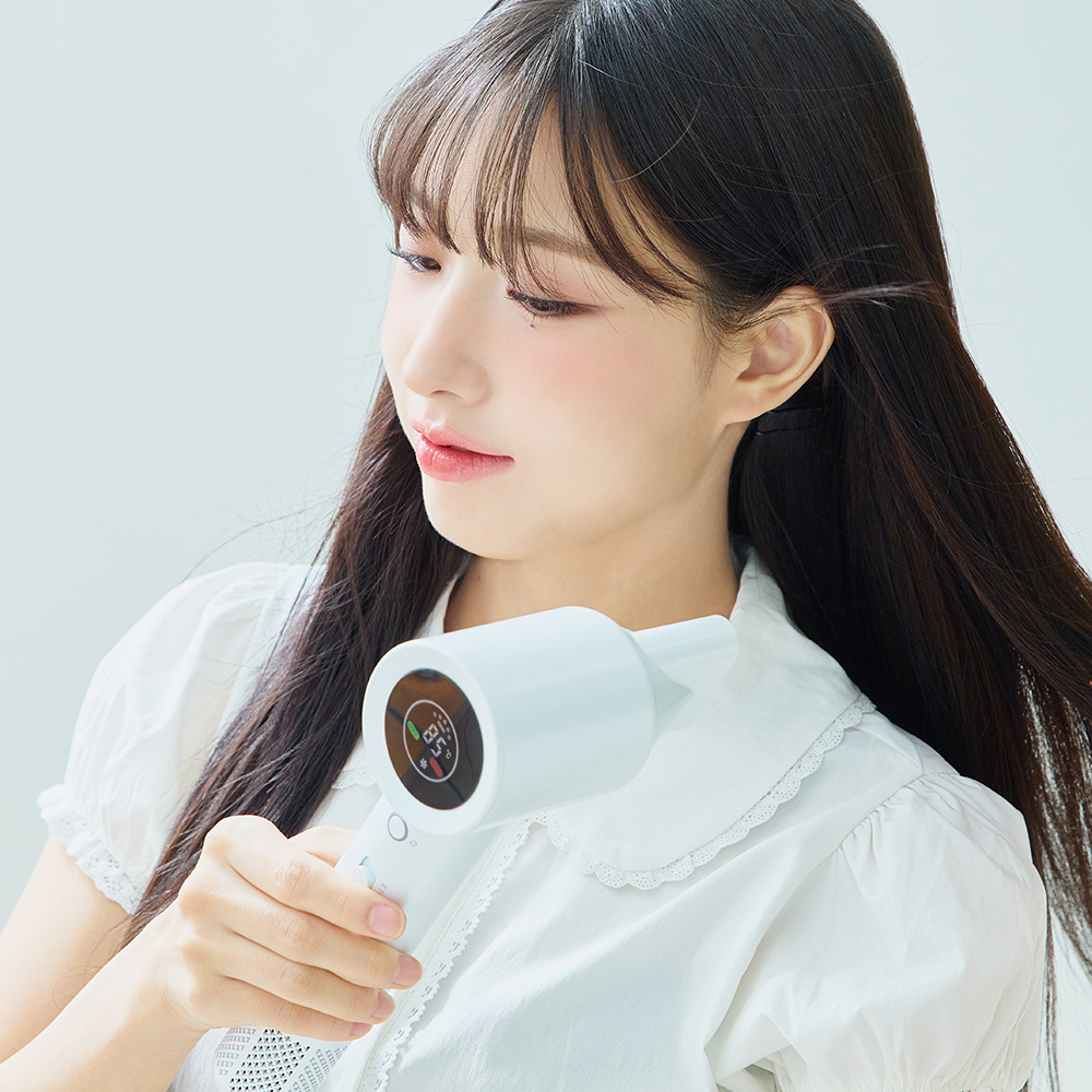 실내에서 드라이기를 들고 있는 여성이 긴 검은 머리에 드라이기를 작동하고 있는 사용 장면