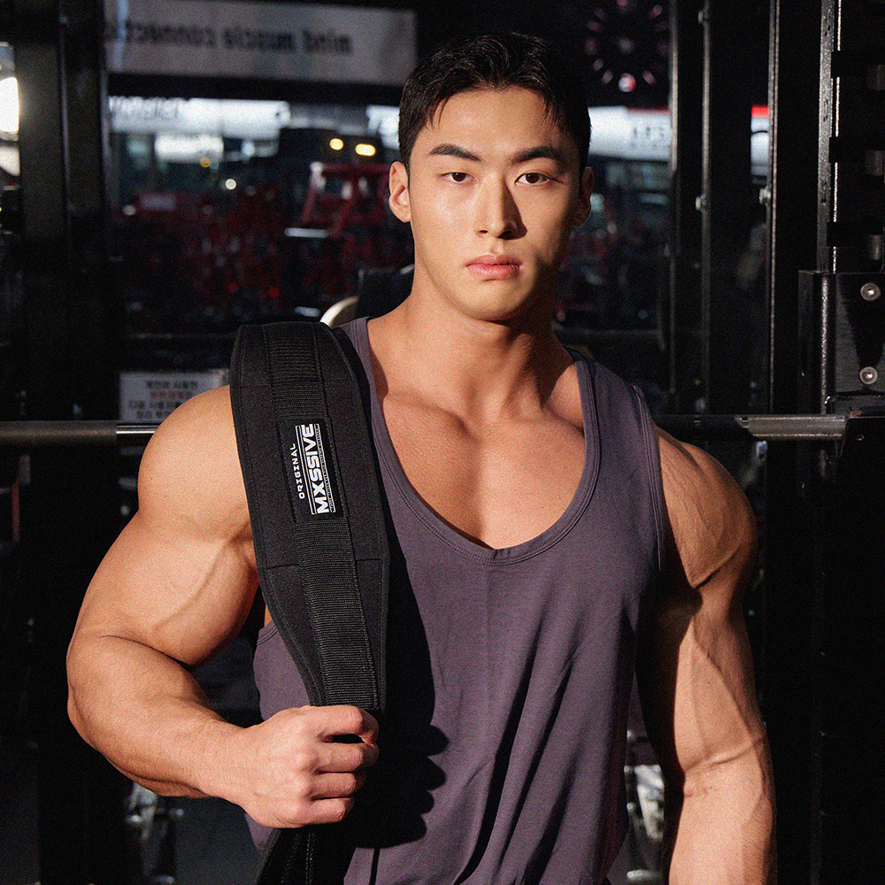 검은 탱크톱을 입은 남성이 헬스장 환경에서 허리에 리프팅벨트를 착용한 모습을 옆면에서 촬영한 사진입니다.