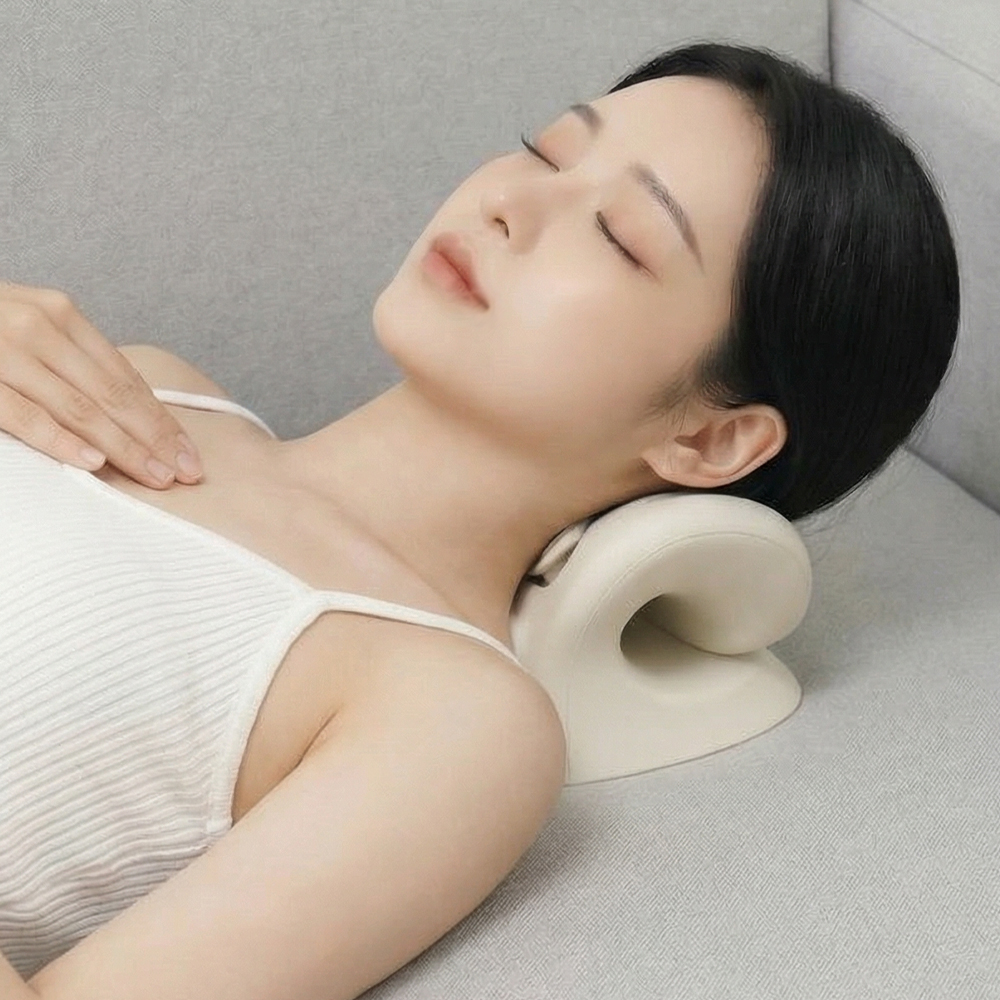 소파에 기대앉은 자세에서 목을 받치며 마사지기를 사용하는 모습으로, 편안한 표정과 함께 기기의 곡선형 형태가 목 부위에 자연스럽게 닿아있습니다.