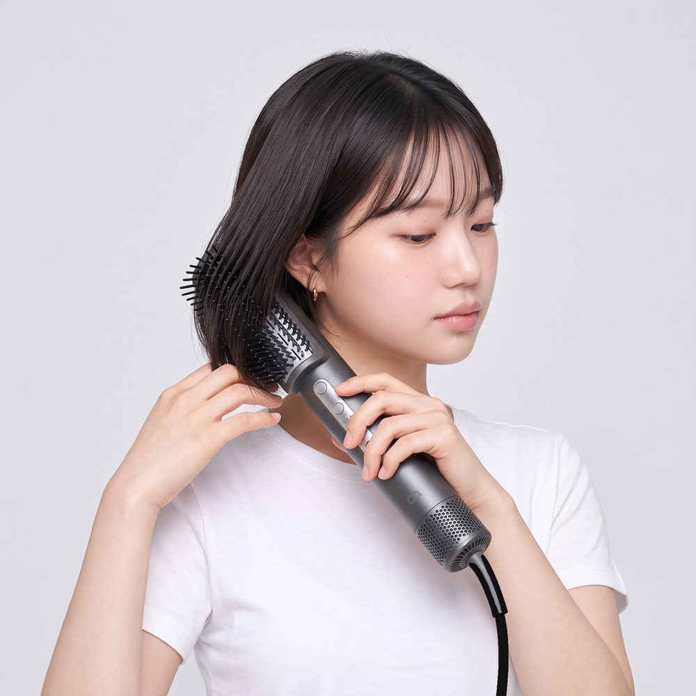 드라이기의 브러시 타입 헤드로 머리를 빗으며 드라이하는 여성의 측면 사진